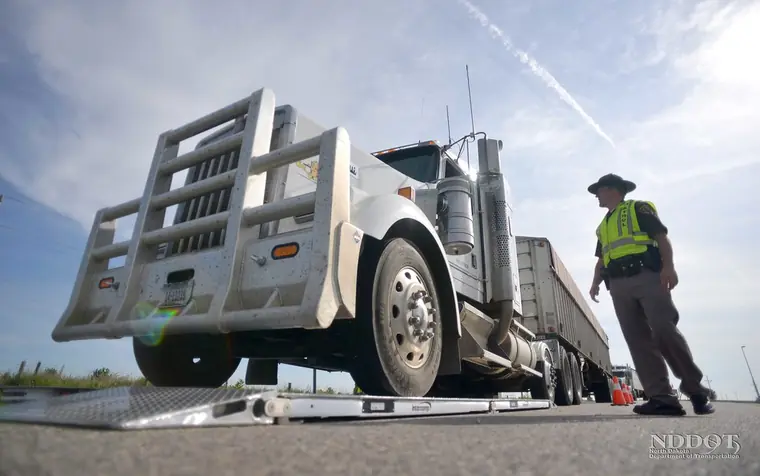 A North Dakota Highway Patrol officer watching a tractor-trailer pull its front axle onto portable scales at a rest area on I-94